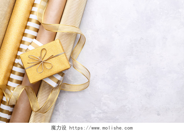 灰色石材背景上金色礼品盒金色光泽包装纸卷和礼品盒